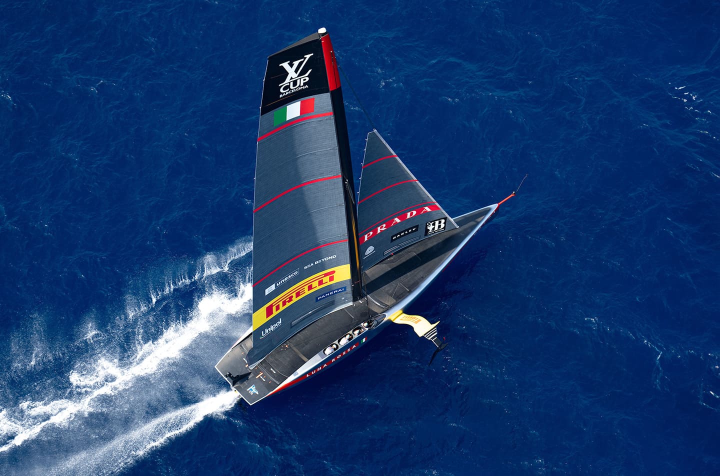 The caravel Luna Rossa sailing on the high seas with the Pirelli logo displayed and cloudy skies in the background.